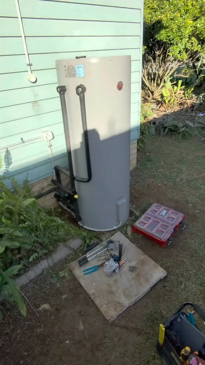 Replacement Rheem 315L hot-water system beside a house, with insulated pipework and new valves